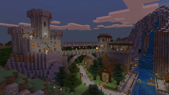 Epic medieval castle build in Minecraft featuring stone towers with orange banners, a bridge connecting structures, and a village pathway next to a waterfall at dusk.